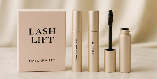 A minimalist lash lift mascara set with two gold tubes and an open wand on a marble counter, styled for an elegant at-home beauty look.