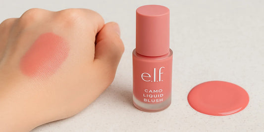 A close-up of e.l.f. Camo Liquid Blush in Pinky Promise, showing the bottle, a swatch on skin, and a soft pink liquid spread on a surface.