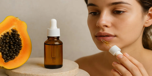 A woman applies papaya seed oil to her lips using a dropper, with a bottle of the oil and a fresh papaya beside her, promoting natural lip care.