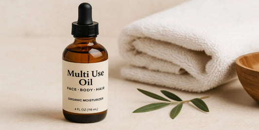 Amber glass dropper bottle of organic multi use oil placed beside a folded towel, wooden bowl, and green leaves in a spa-like setting.