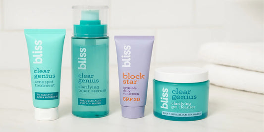 Four Bliss skincare products for acne-prone skin are arranged on a white marble surface with a soft, bright bathroom background.